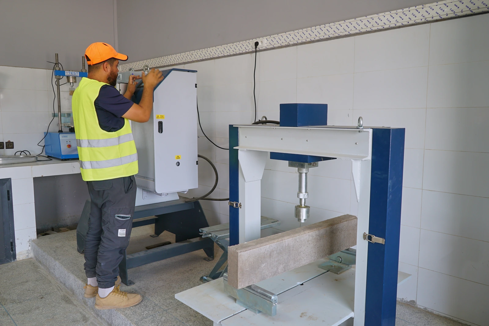 Technicien du laboratoire à la presse de compression, une bordure en béton posée sur le banc de flexion