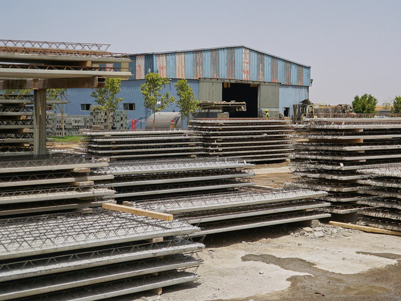 Prédalles en béton à armatures en treillis, stockées en piles sur le parc de l’usine Belza Préfa